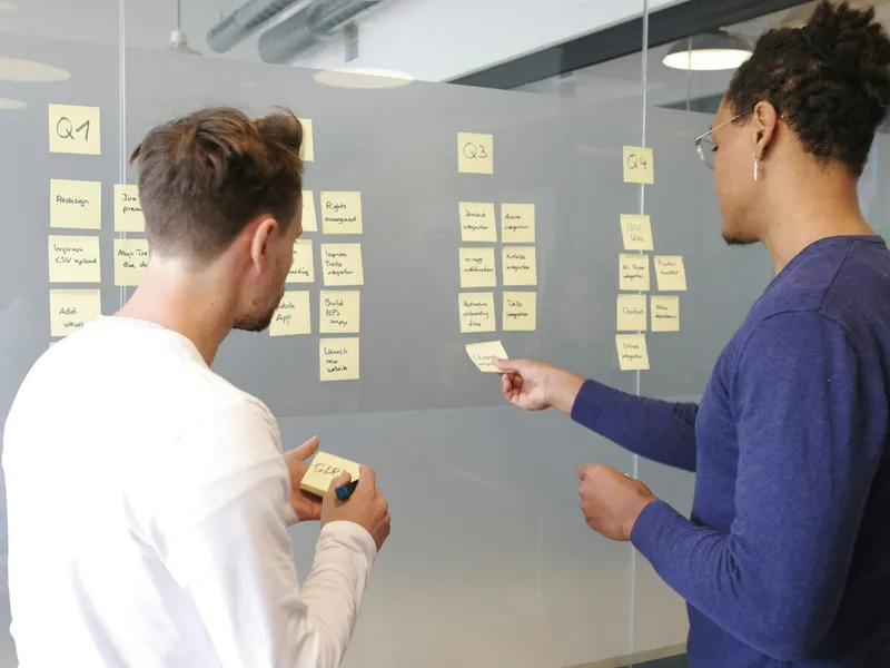 Two people planning a project with sticky notes on a glass wall